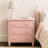 blushed pink nightstand with floral lamp and book next to a bed with floral bedding.