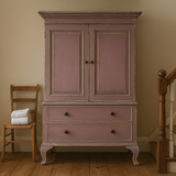 Vintage-style wardrobe with two doors and two drawers in a room with wooden floor and chair.